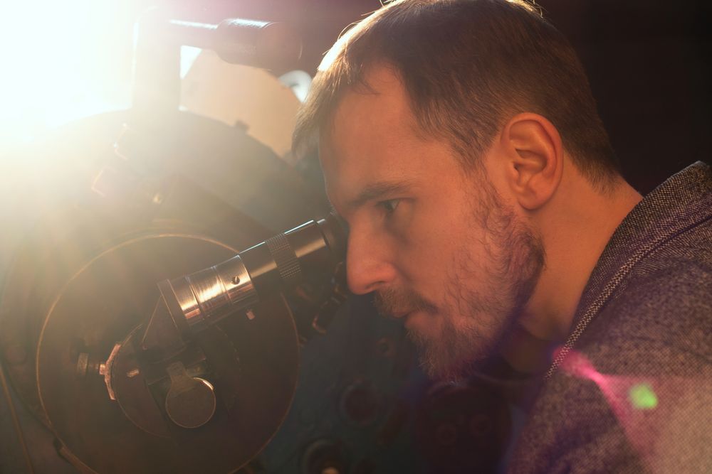 Man peers into telescope, focused on astronomical observation.