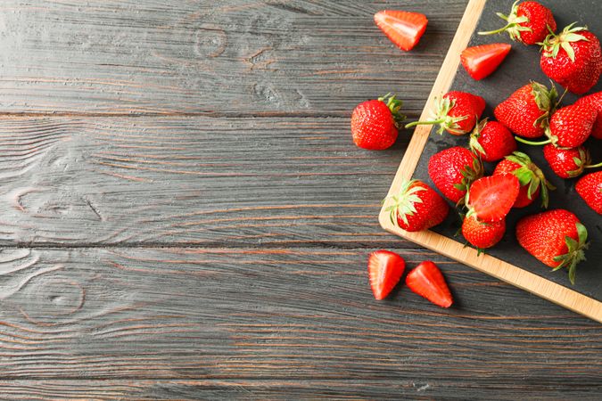 Cutting board and fresh strawberries on wooden table, top view and space for text. Summer sweet fruits and berries