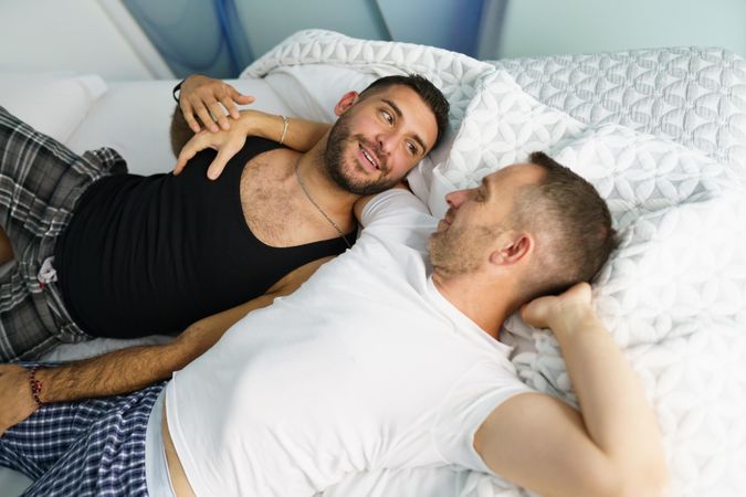 Two males smiling together while lying in bed