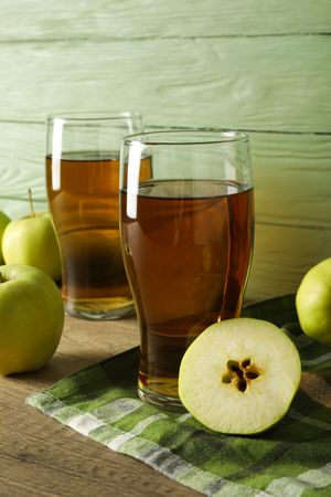 Glasses with apple cider and green apples on wooden table on green wooden background