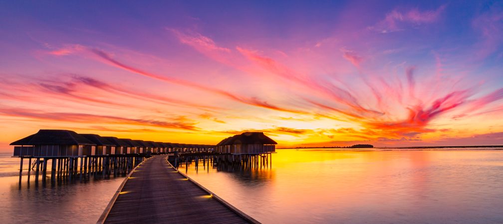 Wooden walkway towards overwater bungalows at sunset, wide shot