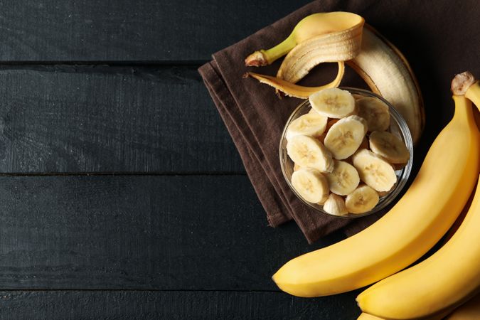 Bowl of banana slices, banana and towel on wooden background