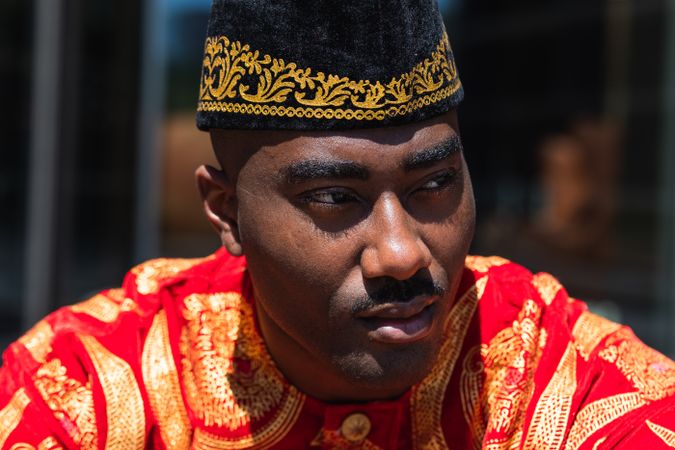 Thoughtful Black man in traditional clothes and headdress near building