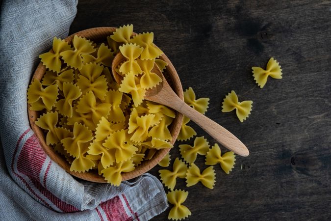 Top view of farfalle pasta in wooden bowl on kitchen counter with kitchen towel