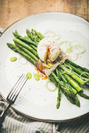 Asparagus and soft boiled egg on plate with fork, on wooden table