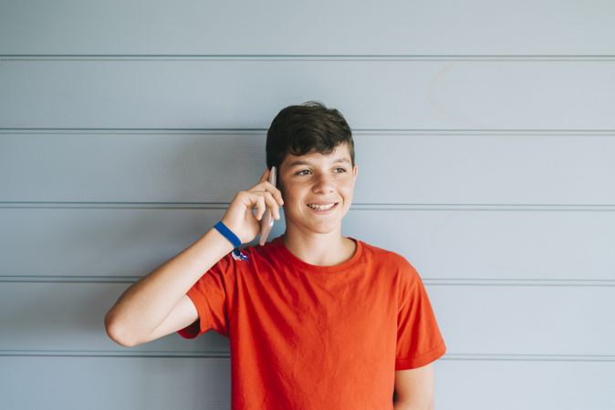 Teenager in red t-shirt standing against wall while using phone