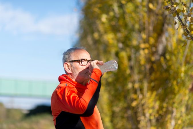 Side view of older man sipping from water bottle in park