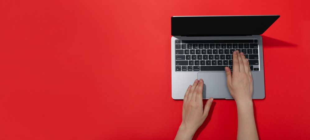 Top view banner of person typing on laptop keyboard on red table with copy space