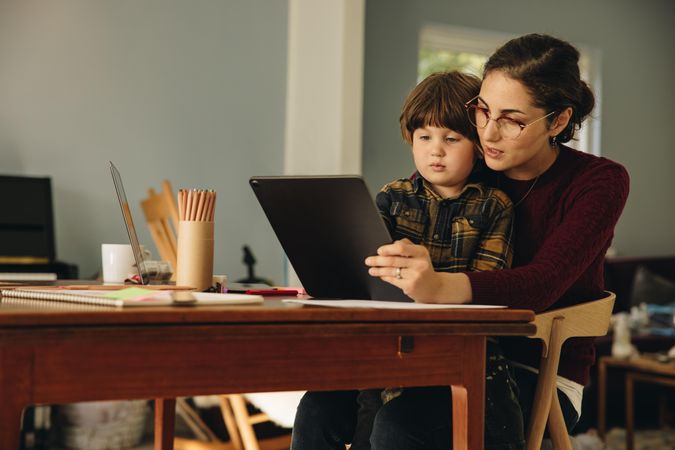 Woman and son sitting at table using digital tablet