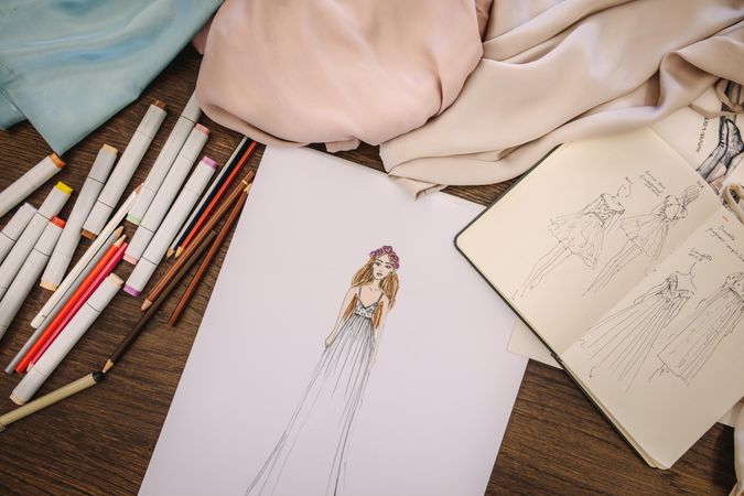 Fashion design sketches, dress materials and drawing pens on a table