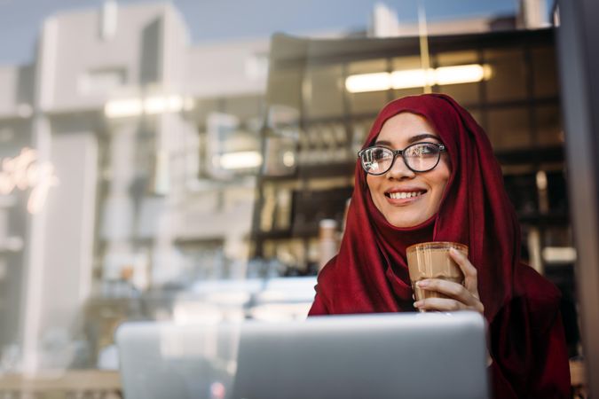 Smiling Muslim woman wearing hijab and eyeglasses relaxing at cafe