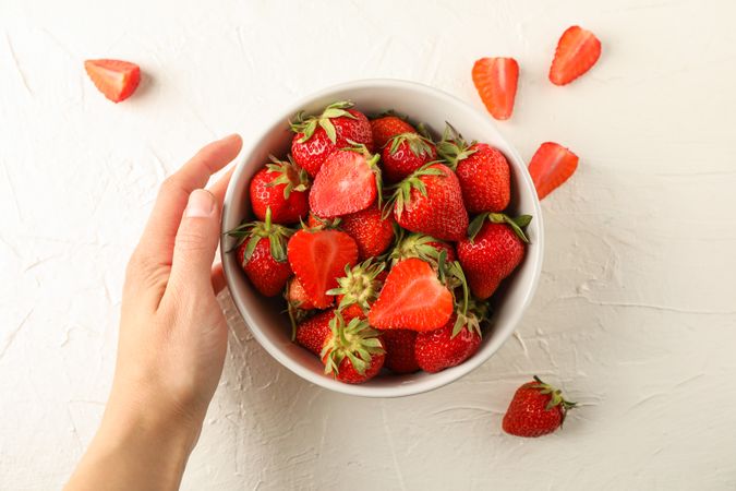 Female hand hold bowl with fresh strawberries on light background, space for text. Summer sweet fruits and berries