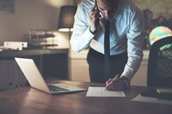 Professional man writing on documents while on a cell phone
