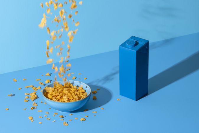 Pouring cornflakes cereal in a bowl on a blue table