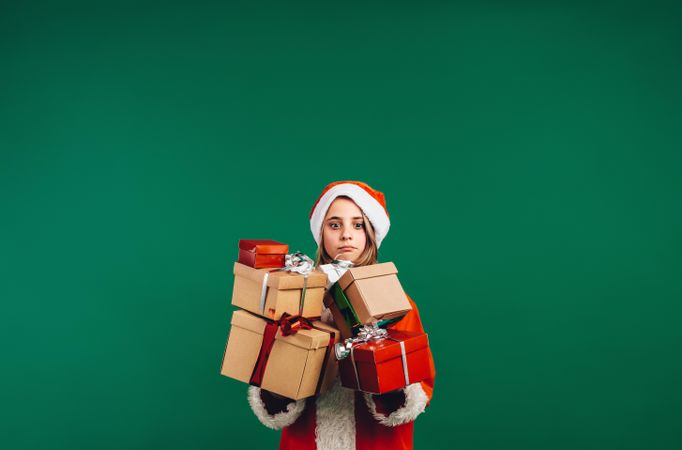 Worried girl dressed in Santa suit carrying heavy gift boxes