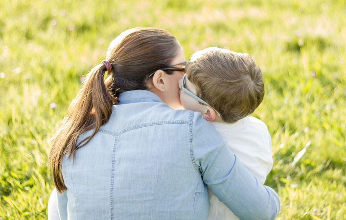 Cute son kissing to his mother sitting in a field