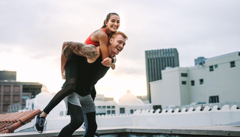 Athlete carrying a fitness woman on his back and walking on rooftop