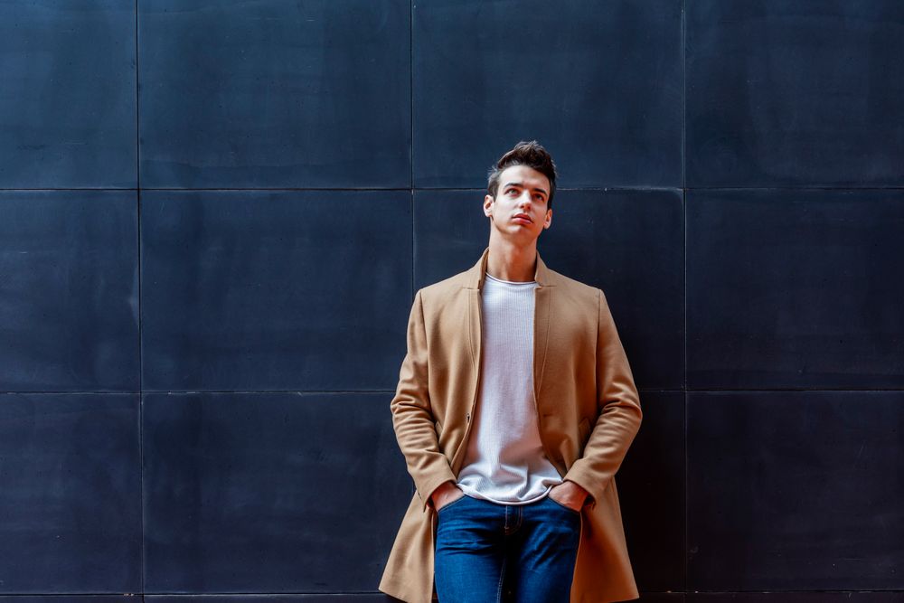 Young man in the center wearing winter coat looking up against dark wall