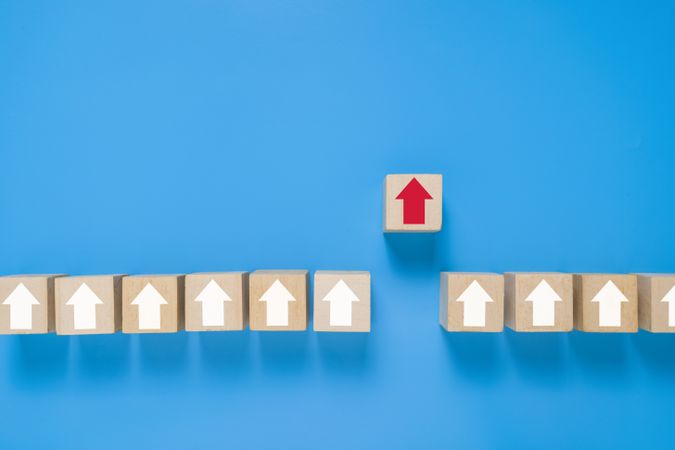 arrows and single red arrow pointing up on wooden blocks isolated on blue background. concept of leadership