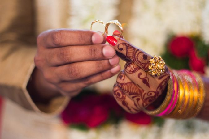 Close-up shot of woman's hands with mehndi tattoo holding two rings