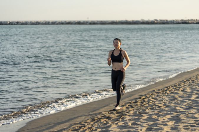 Sportswoman running on sandy sea beach on sunny day
