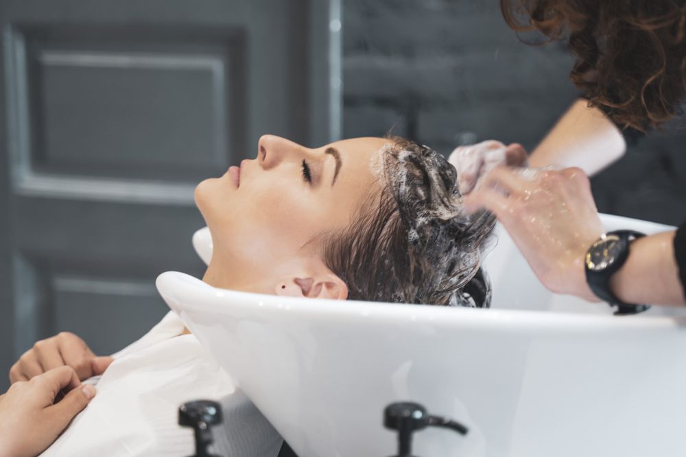Stylist washing hairs to young lady