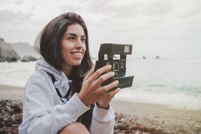 Woman with camera on shore near stones and water