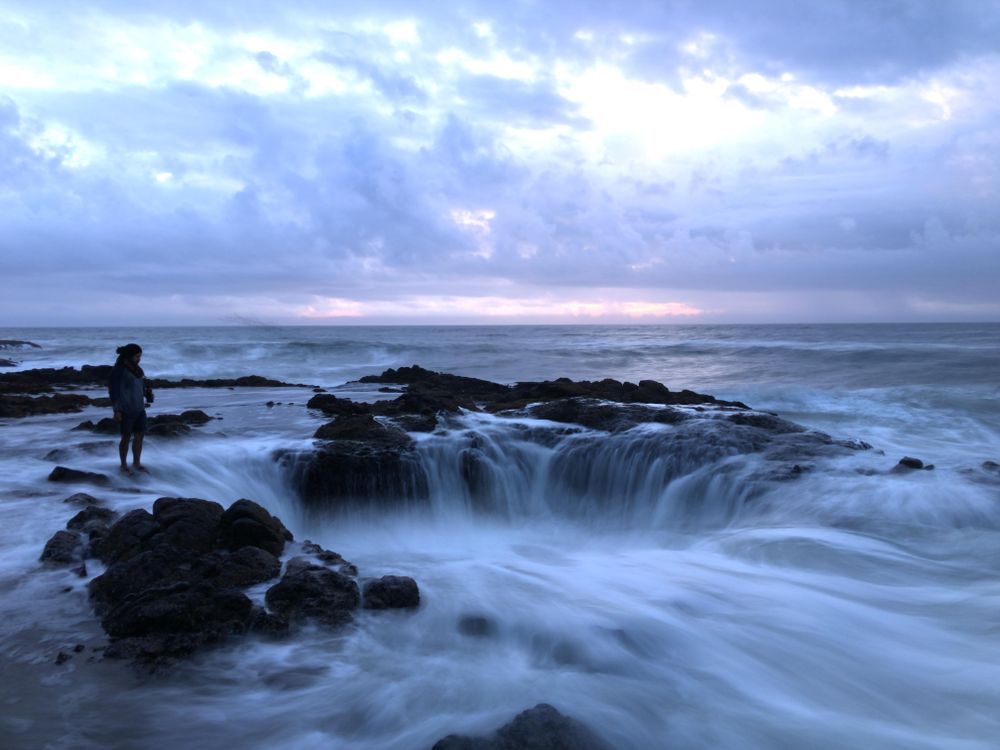 Person standing on seashore near hole in sea under cloudy sky