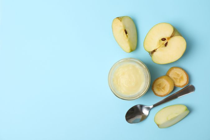 Glass jar with apple puree on blue background, top view