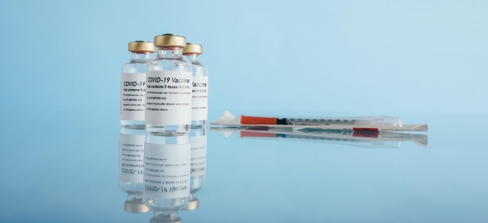 Covid-19 vaccine vials and syringe on reflective surface