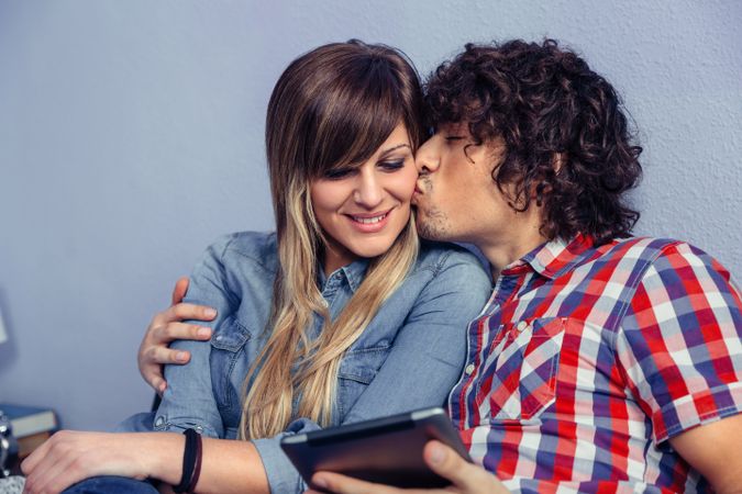 Man kissing woman while holding tablet
