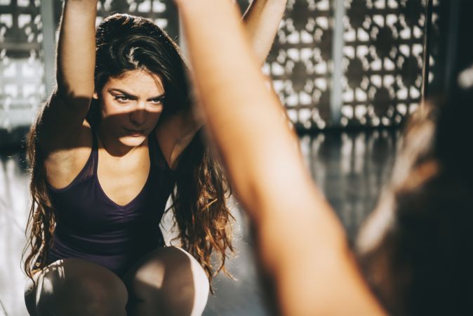 Concentrated brunette in ballet class warming up while looking at mirror in sunlight.