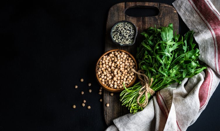 Top view of bowl of garbanzo beans and sesame seeds next to arugula 