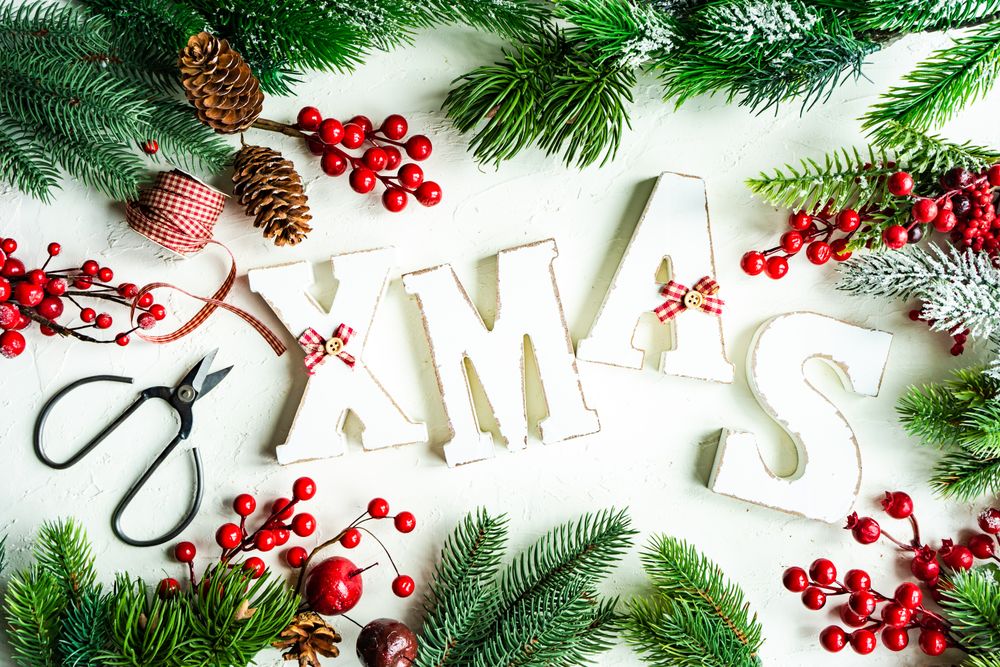"XMAS" surrounded by green wintry branch with red decorations, scissors and ribbon