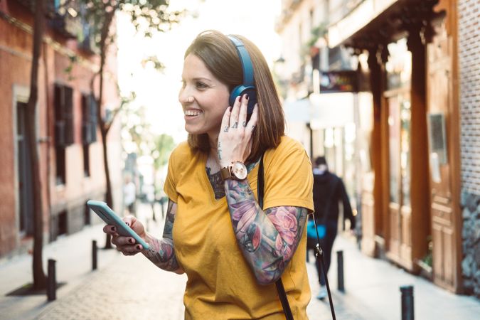 Inspired woman in headphones listening to music on smartphone on street