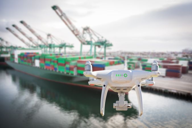 Unmanned Aircraft System Quadcopter Drone In The Air Near Large Shipping Vessel and Dock with Crates