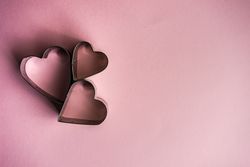 Three heart shaped cookie cutters on pink background