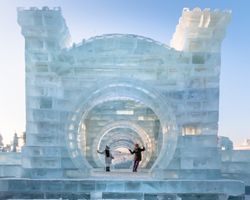 man and woman in warm outwear standing standing on illuminated castle of ice and snow