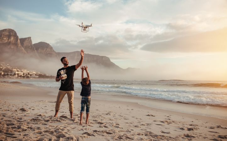 Happy father showing his son how to fly a drone at beach
