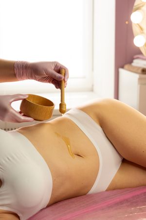 Warm honey poured across stomach during wellness body care session.