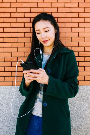 Asian female listening to music near brick wall