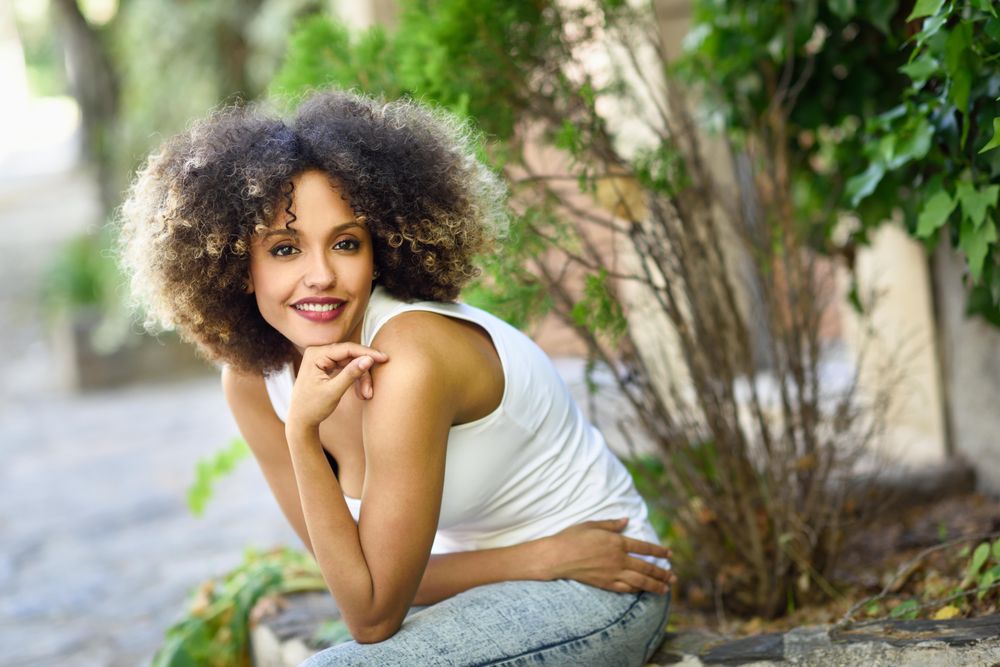 Young Black woman with afro hairstyle smiling while sitting outside