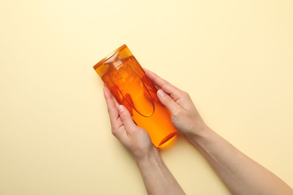 Female hands hold shampoo bottle on beige background, space for text