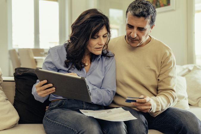 Woman holding a digital tablet and man holding a credit card to pay bills online.