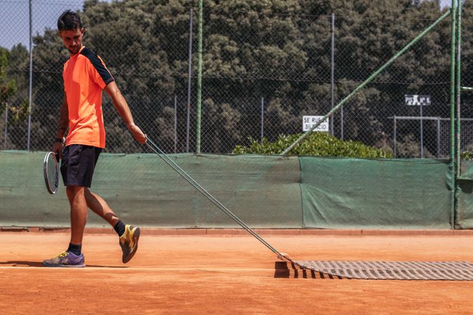 Man playing tennis doing court maintenance