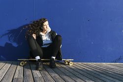 Teenage girl sitting on a longboard, leaning against a blue wall