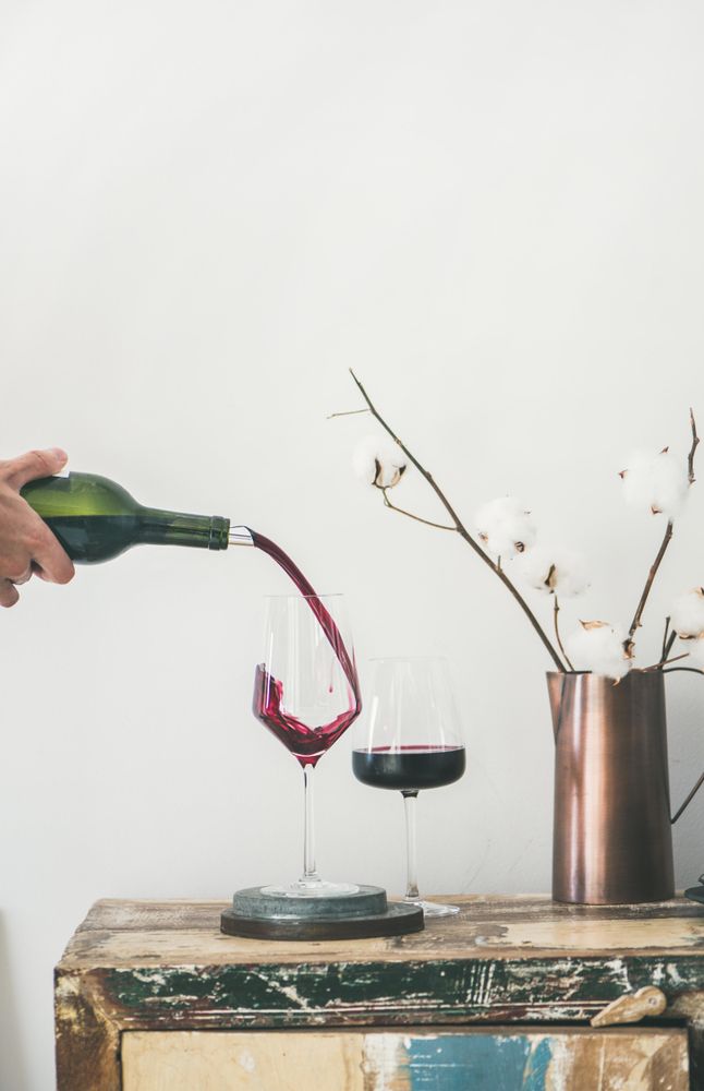Wine glasses being poured from bottle with dried cotton in vase, vertical composition, copy space