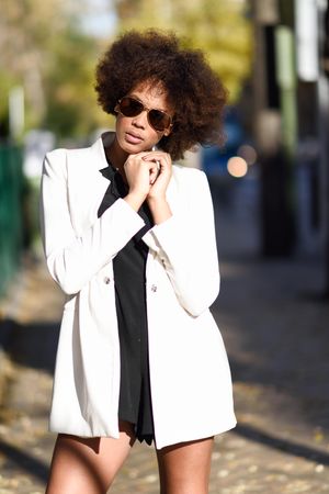 Female in short dress and blazer standing in the sun with hands clasped