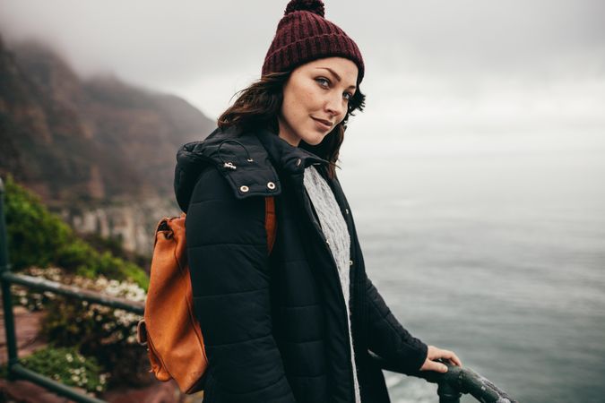 Portrait of beautiful young woman standing by a railing at hill top and looking at camera