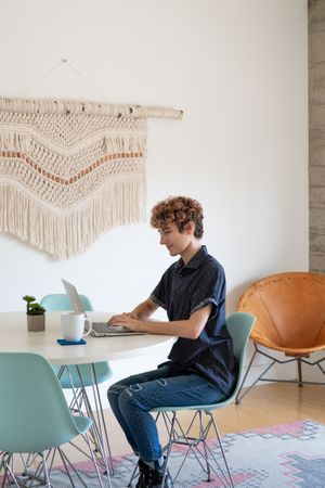 Nonbinary person working at table with macramé on the wall